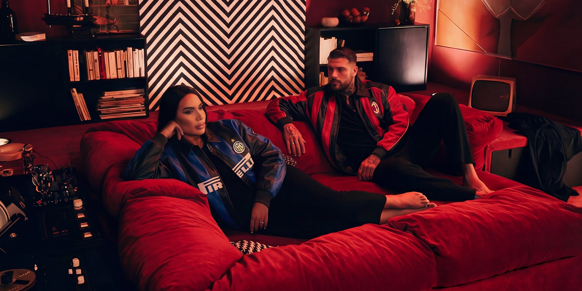Two people sitting on a red couch in a room with a geometric wall pattern. Bomber jackets by Eternal Core.