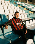 Pessoa a usar uma camisola desportiva com logótipo de marca sentada num estádio vazio.